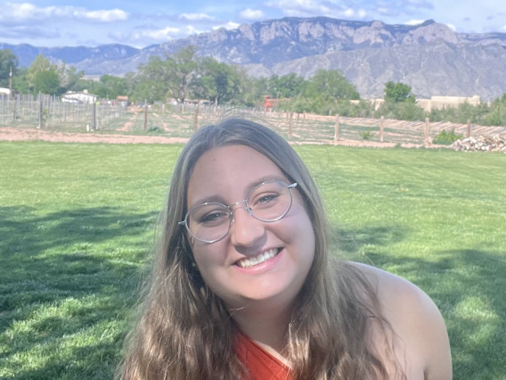 Andreanna Roros, graduate student in a grassy field with mountains in the distant background