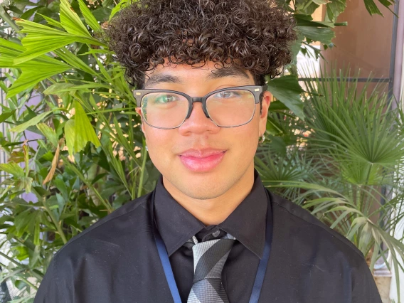 person in dress clothes and glasses in front of greenery