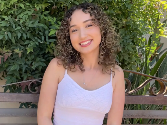 a person sitting on a park bench in front of greenery.