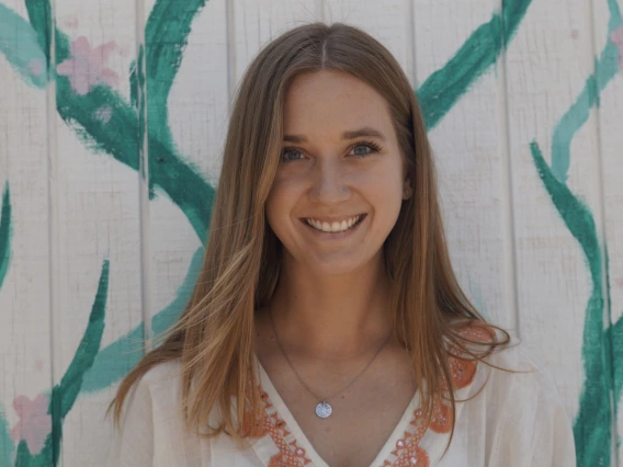 a photo of a person smiling in front of a white wall painted with flowers