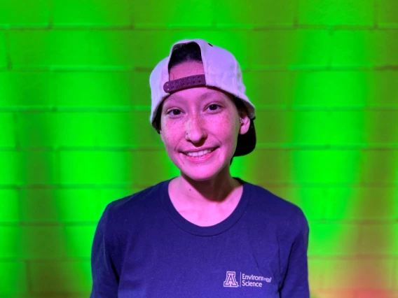 photo of a person in a University of Arizona Department of Environmental Science shirt in front of a green lighted brick wall