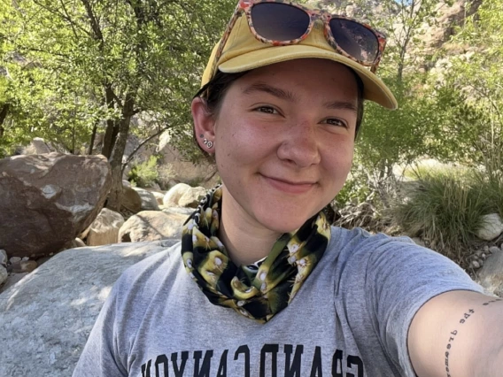 photo of a person in hat and bandana in front of rocks and greenery