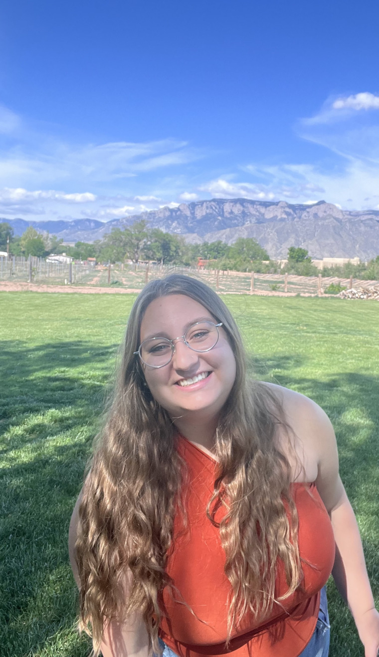 Andreanna Roros, graduate student in a grassy field with mountains in the distant background