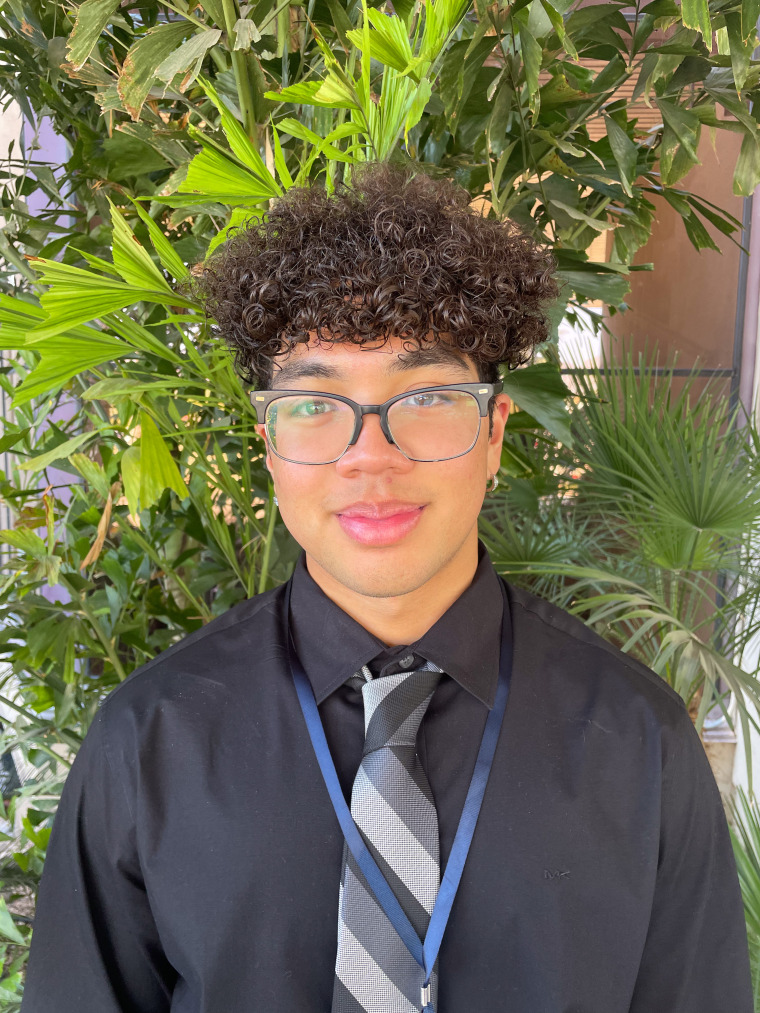 person in dress clothes and glasses in front of greenery