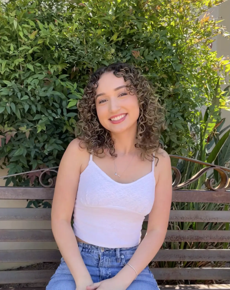 a person sitting on a park bench in front of greenery.