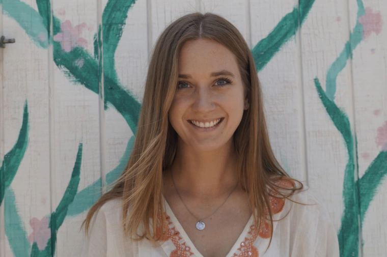 a photo of a person smiling in front of a white wall painted with flowers