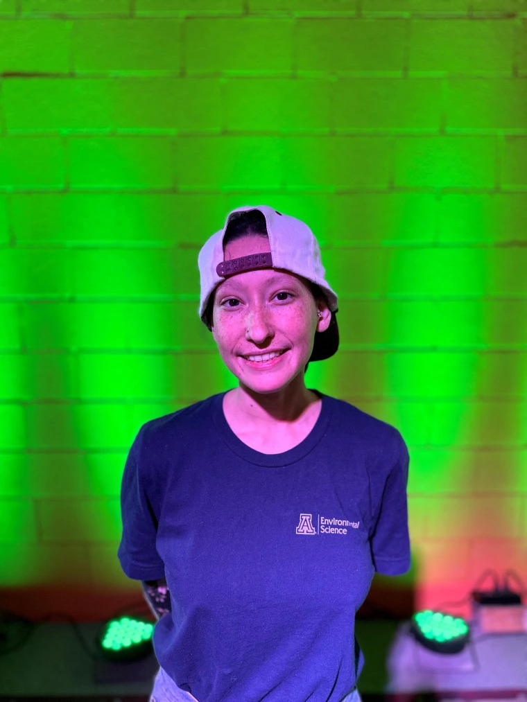 photo of a person in a University of Arizona Department of Environmental Science shirt in front of a green lighted brick wall