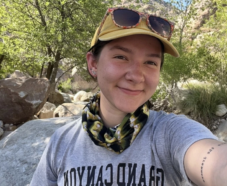 photo of a person in hat and bandana in front of rocks and greenery