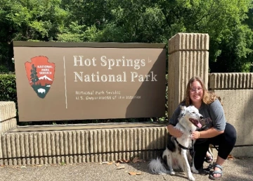 a photo  of a person and a dog in front of a sign that reads "Hot Springs National Park"