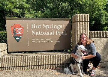 a photo  of a person and a dog in front of a sign that reads "Hot Springs National Park"