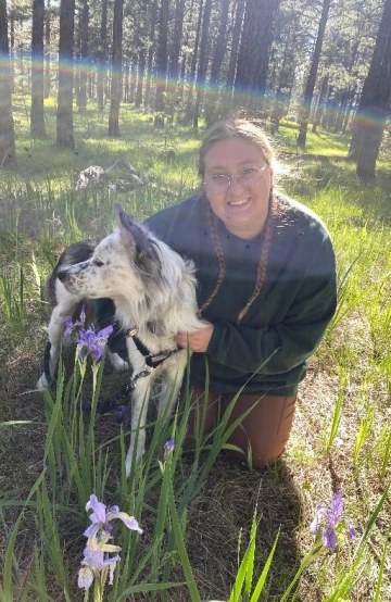 Andreanna Roros, graduate student with a white dog in a grassy forest.